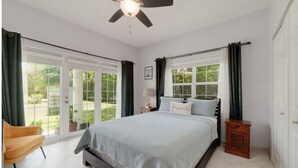 A bedroom with a bed, a chair, a nightstand, and a ceiling fan.