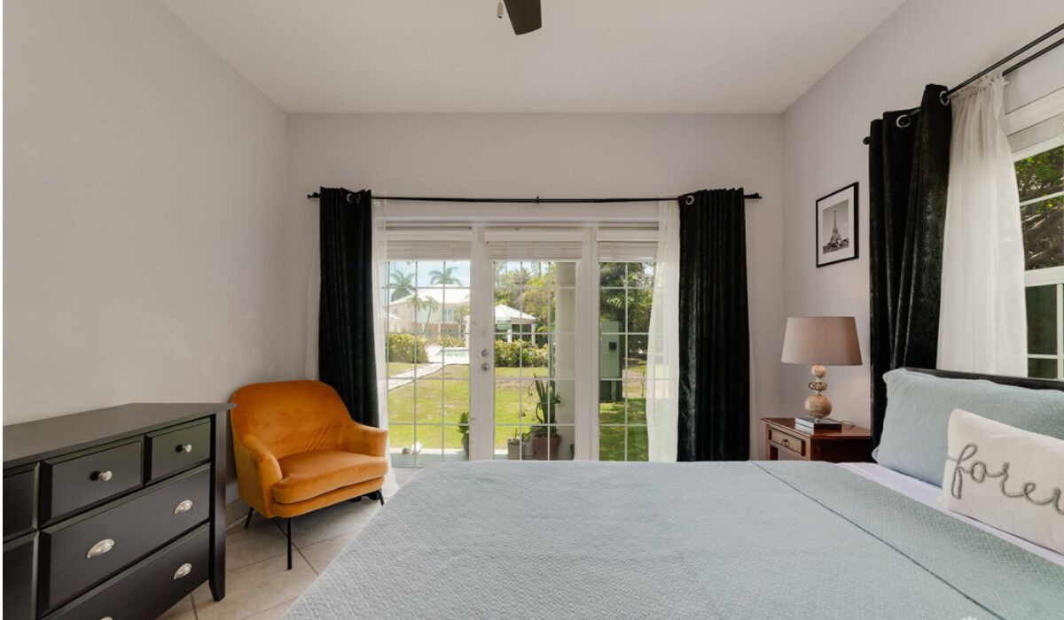 Un dormitorio con cama, mesita de noche, lámpara, silla y cómoda.