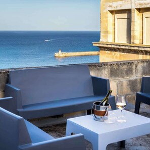 A terrace with a table set for two, overlooking a body of water with a pier. - 123 St Ursula Street (Il-Belt Valletta)