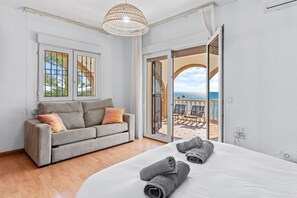 Un dormitorio con cama, sofá gris, ventana con vistas y balcón con vistas.