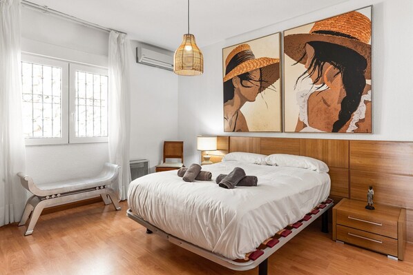 Un dormitorio con cama, mesitas de noche, una silla y una obra de arte en la pared.