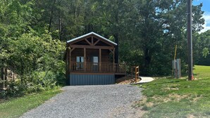 Eine Holzhütte mit Veranda, umgeben von Bäumen und einem Kiesweg, der dorthin führt.