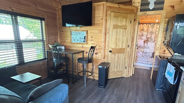 Ein Holzblockhaus-Interieur mit Sofa, Esstisch, Stühlen, einem Fernseher und einer Küchenzeile.