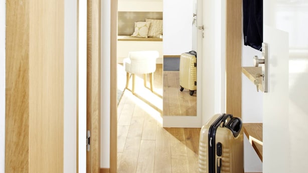 A hotel room with a wooden floor, a white bed, a small table, and a suitcase. - KÖNIGSschlafs cuddly nest for 2 persons with sunny balcony (Konstanz)