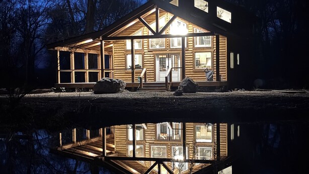 Une cabane en rondins dotée d’une grande terrasse et dont le reflet se mire dans l’eau.