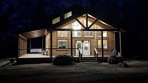 Une cabane en rondins dotée d’une grande véranda à l’avant, de nombreuses fenêtres et d’un toit en pente.