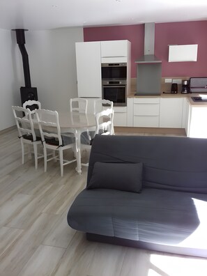 Ein modernes Wohnzimmer mit einer Couch, einem Esstisch, Stühlen, einer Küchenzeile mit Schränken und Geräten sowie einem Kamin.
