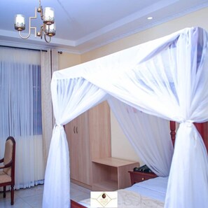 A hotel room with a bed covered in white drapes, a wooden nightstand, a chair, and a wardrobe.