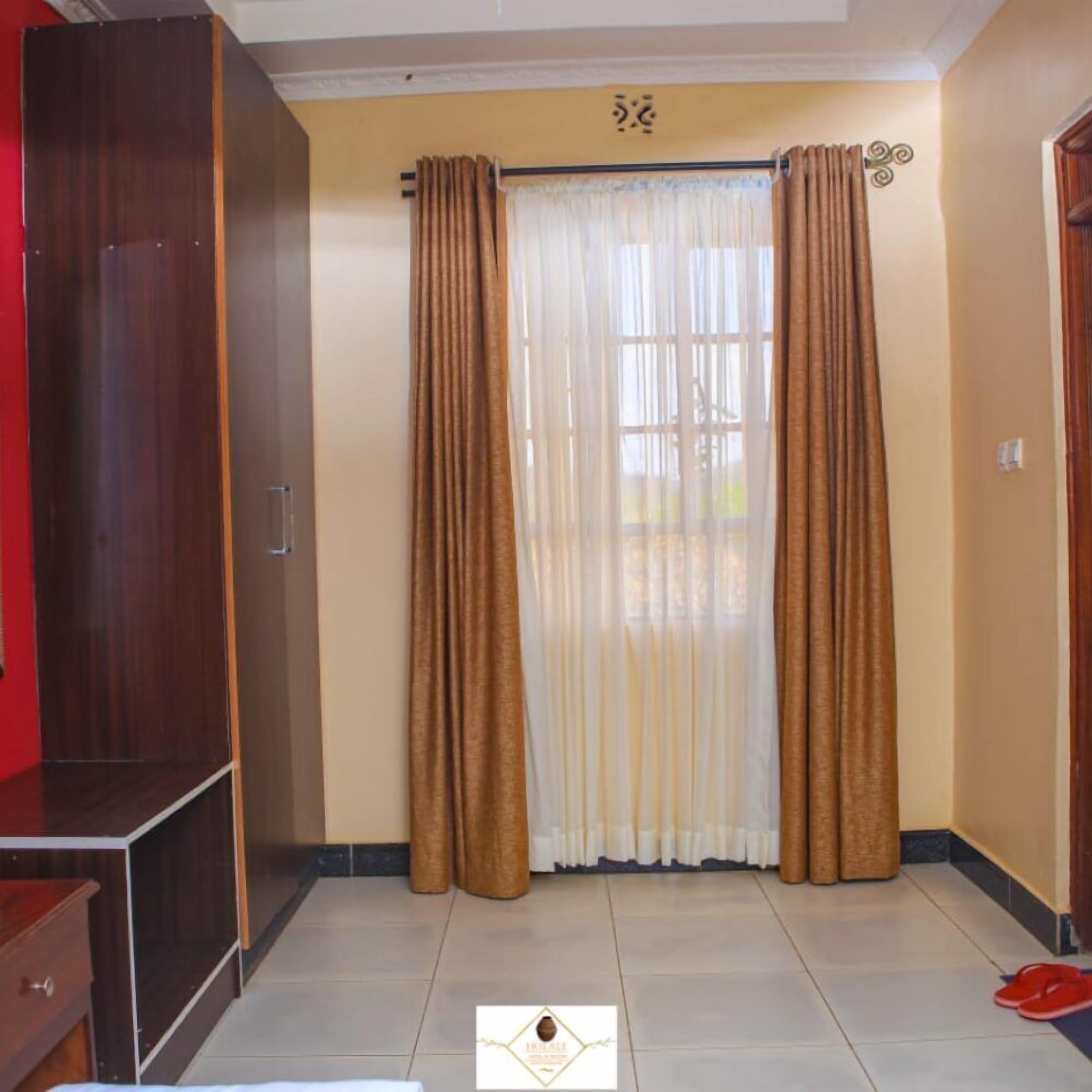 A room with a wardrobe, a window with curtains, and a tiled floor.