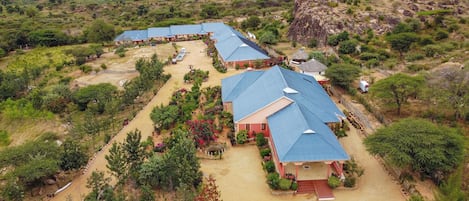 A hotel with multiple buildings, each with a blue roof, surrounded by greenery and a hilly landscape.
