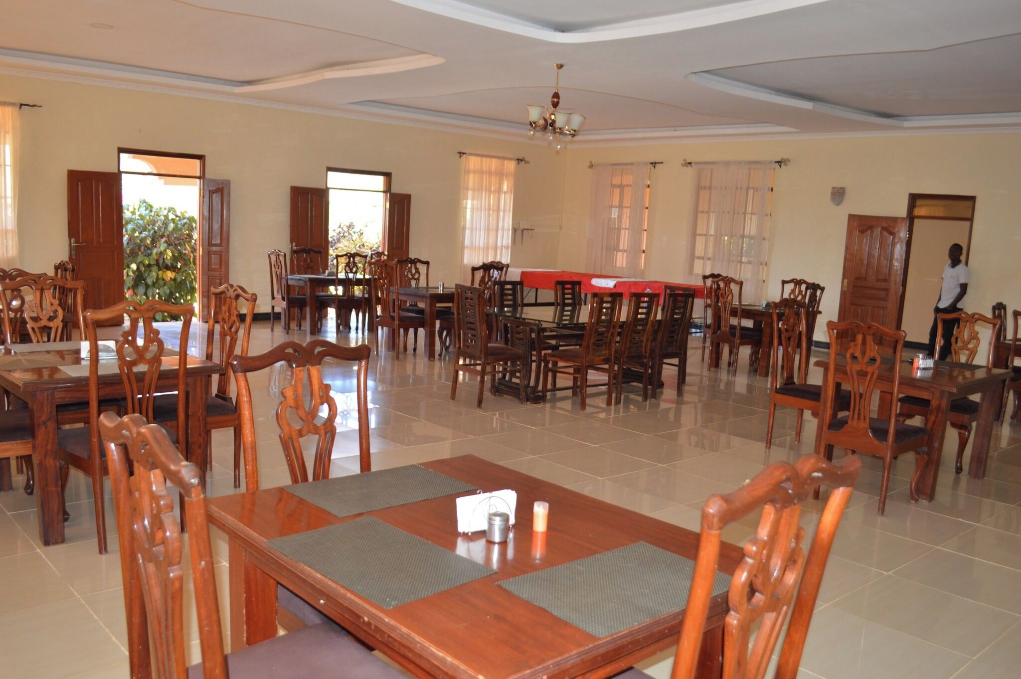 A spacious dining area with multiple wooden tables and chairs, large windows, and a chandelier.