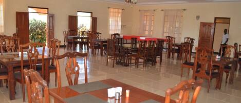 A spacious dining area with multiple wooden tables and chairs, large windows, and a chandelier.