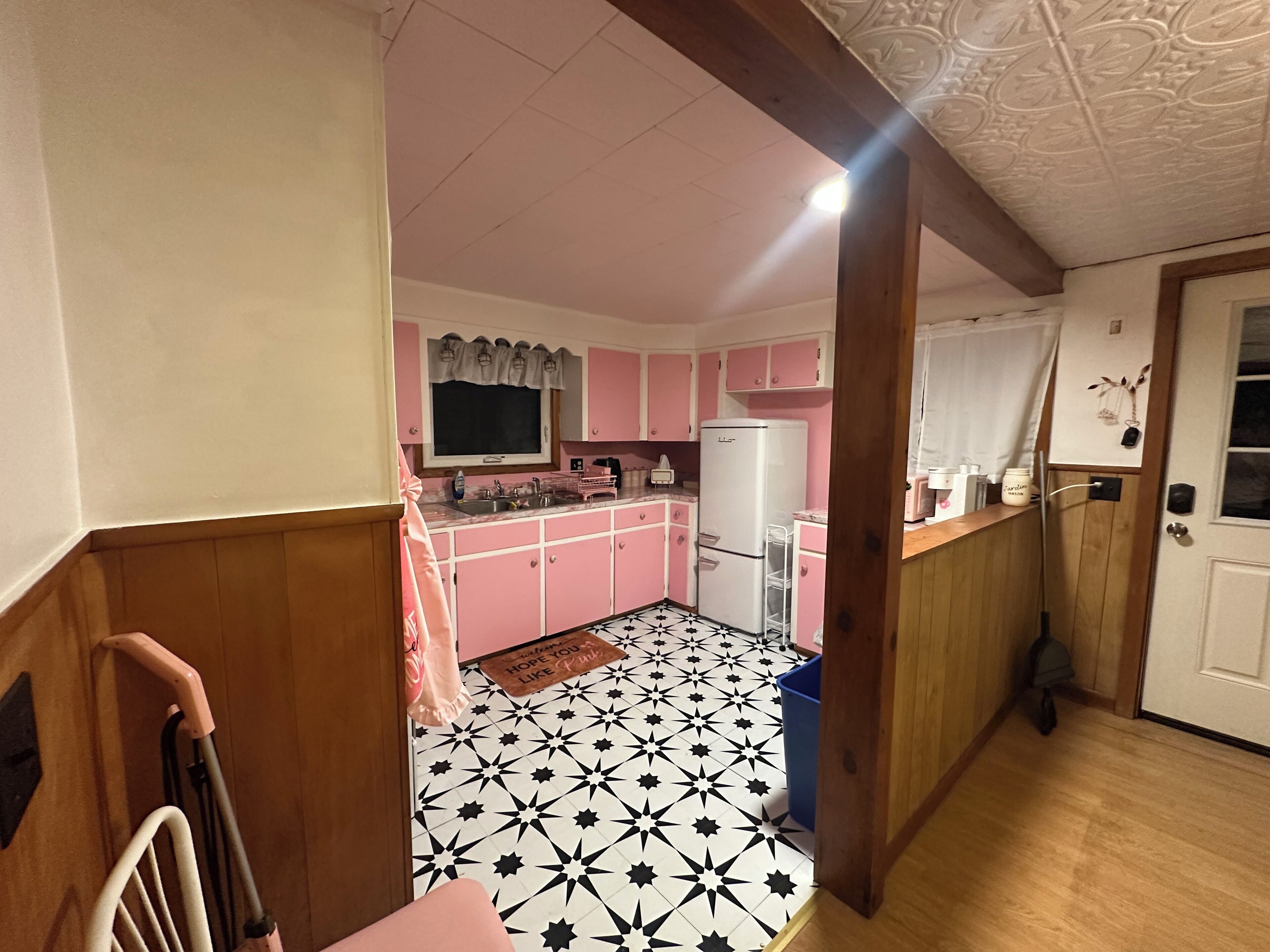 A kitchen with pink cabinets, a white refrigerator, and a black and white star-patterned floor.