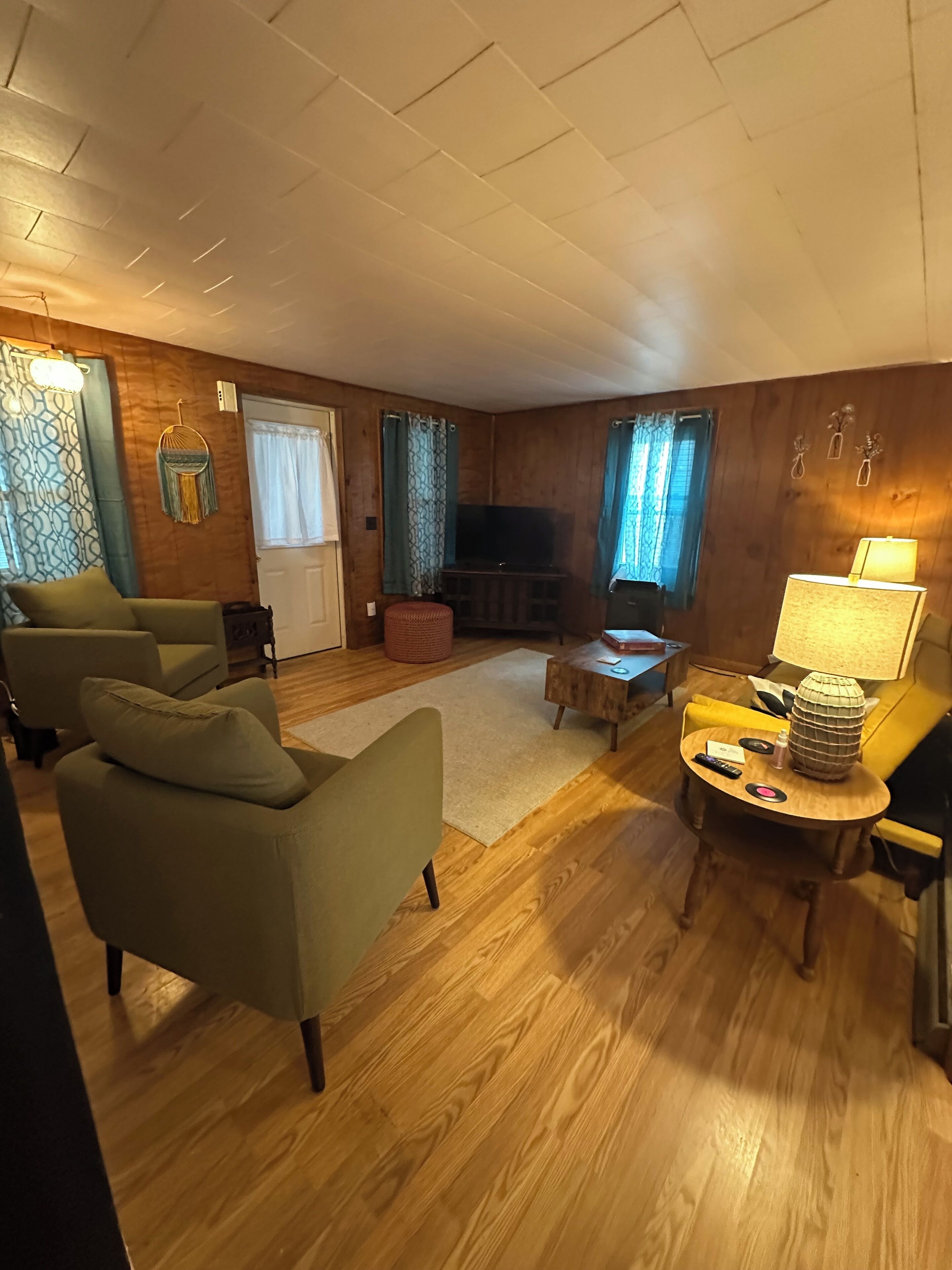 Una sala de estar acogedora con paredes de madera, un televisor de pantalla plana, una mesa de centro redonda de madera y dos sillones verdes.