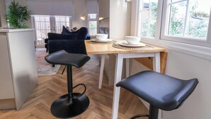 A modern kitchen with a wooden table, two black bar stools, and a view of the outside through large windows. - Lodge (Holywell)