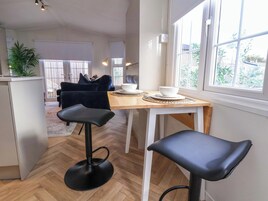 A modern kitchen with a wooden table, two black bar stools, and a view of the outside through large windows.