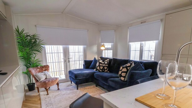 A modern living room with a blue sofa, a coffee table, and a bar area with two glasses. - Lodge (Holywell)
