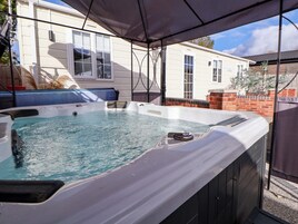 A hot tub under a canopy with a view of a house and a brick wall.