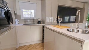 A modern kitchen with white cabinetry, a stainless steel sink, a wooden cutting board, and a coffee maker. - Lodge (Holywell)