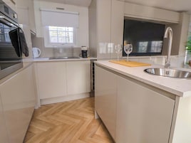 A modern kitchen with white cabinetry, a stainless steel sink, a wooden cutting board, and a coffee maker.