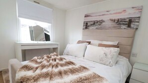 A bedroom with a bed, a bedside table, a desk, and a painting on the wall. - Lodge (Holywell)