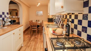Een kleine keuken met houten kastjes, een gasfornuis, een spoelbak en een eethoek met stoelen en een tafel.