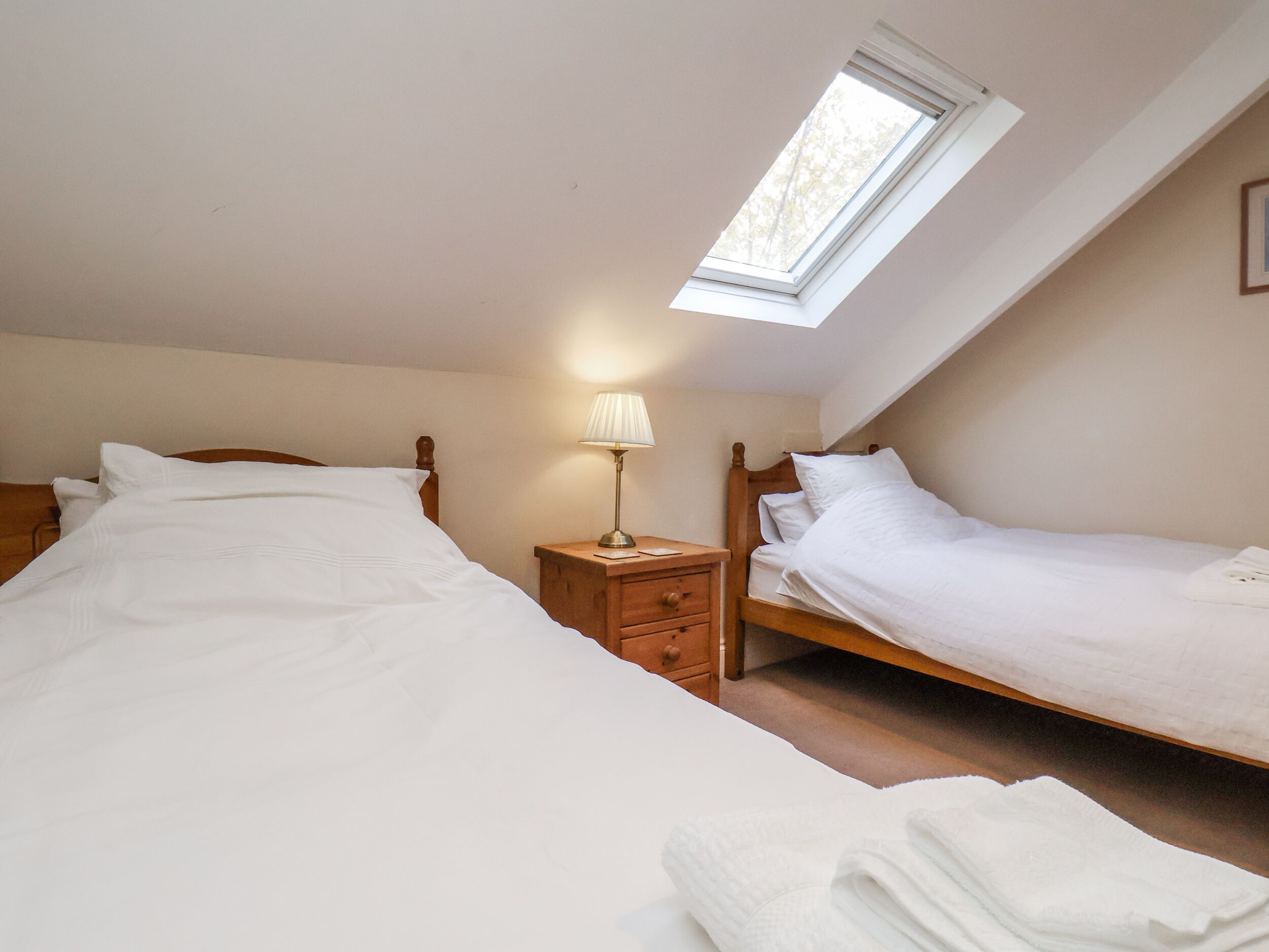 Een slaapkamer met twee eenpersoonsbedden, een nachtkastje met een lamp en een dakraam.