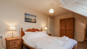 Een slaapkamer met een houten bed, twee nachtkastjes met lampen, een schilderij aan de muur en een houten garderobe.