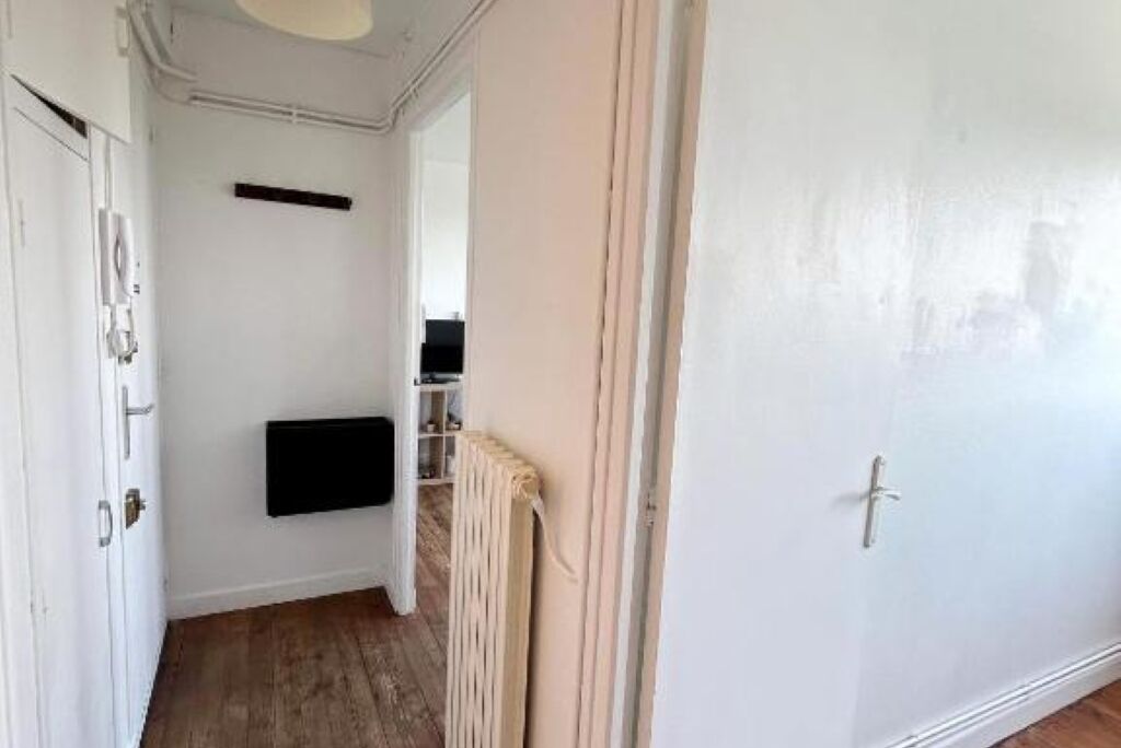 Un couloir avec une porte blanche, un radiateur et une étagère noire.
