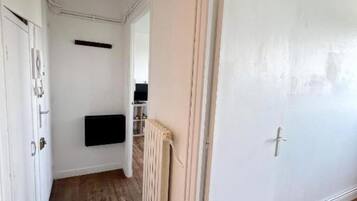 Un couloir avec une porte blanche, un radiateur et une étagère noire.