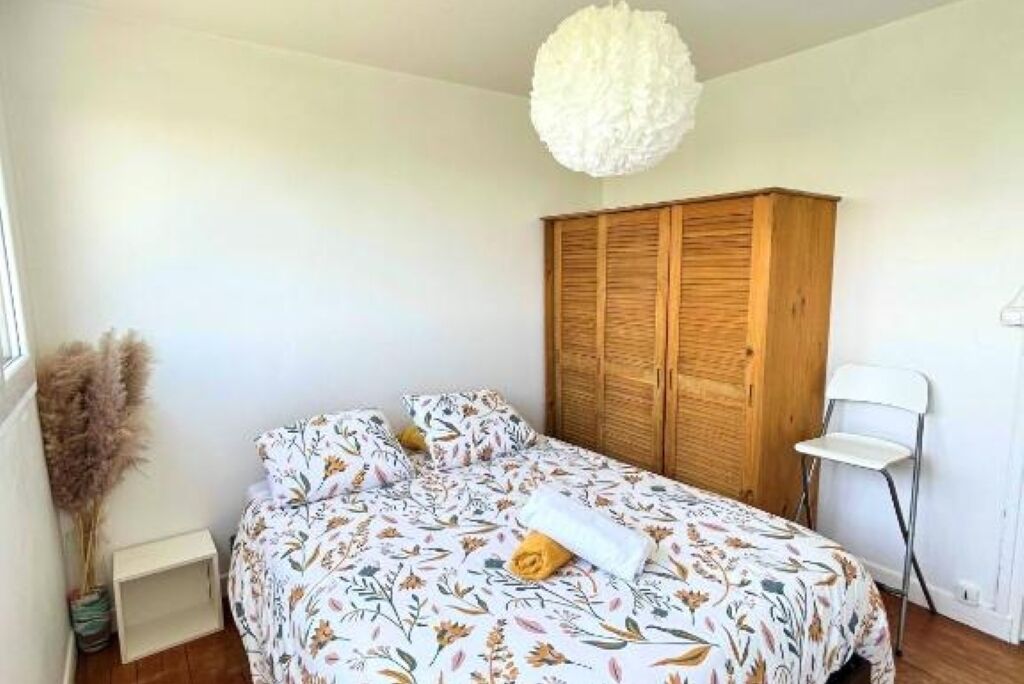 Une chambre à coucher avec un lit, une armoire en bois, une chaise blanche et un luminaire suspendu.