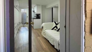 Ein kompakter Raum mit einer Küchenzeile, einem Bett mit weißer Decke und einer Tür zu einem weiteren Raum.