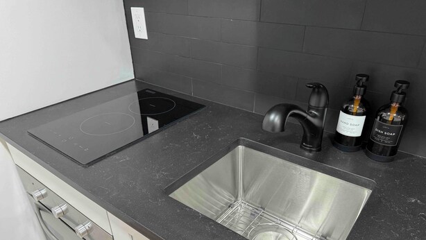 Eine moderne Küche mit schwarzem Arbeitsplatz, Spüle aus Edelstahl und zwei Flaschen Geschirrspülmittel.
