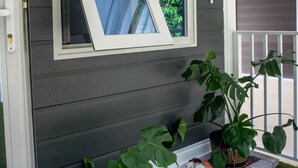 Ett hus med en grå fasad, ett vitt fönster och en liten trädgård med växter och vita stenar.
