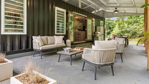 Un espace extérieur aménagé, abrité et doté d’un canapé, de fauteuils, d’une table basse et de jardinières.
