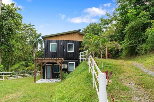 A two-story house with a wooden exterior, a porch, and a white fence. - Vagones del Río | River Access | Sleeps 8 (Rincón)