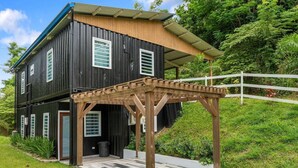 Une maison à deux étages avec une terrasse en bois et une clôture blanche.