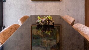 A conference table with a glass top, surrounded by woven chairs, against a concrete wall with a framed painting above. - Casa Gama Gabriel | Art and Design in Northern Rome (Ciudad de México)