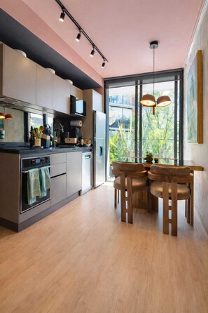 A modern kitchen with a dining area, large windows, and a view of greenery.