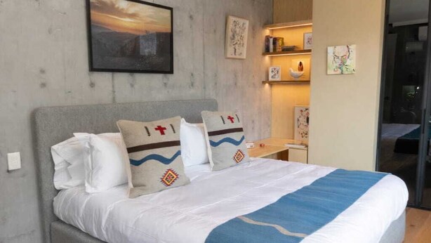 A modern bedroom with a grey bed, white bedding, and a blue throw blanket. There is a colorful rug on the floor and a painting on the wall. - Casa Gama Gabriel | Art and Design in Northern Rome (Ciudad de México)