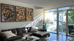 Ein modernes Wohnzimmer mit Ledersofa, abstrakter Kunst an der Wand und Blick durch große Glasfenster.