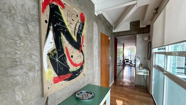 Ein Flur mit modernem Design, der eine Betonwand mit abstrakter Kunst, einen Holzboden und einen Blick durch ein großes Fenster zeigt.