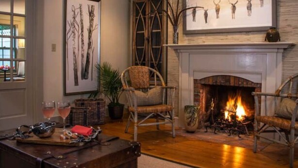 A cozy living room with a fireplace, wicker chairs, and a coffee table with snacks. - Deer Brook Inn  (Woodstock)
