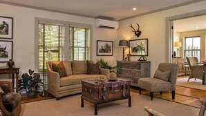 A living room with a beige sofa, a wooden coffee table, and a fireplace. There are framed pictures on the walls and a lamp on a side table. - Deer Brook Inn  (Woodstock)