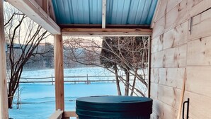 A wooden deck with a hot tub, a wooden chair, and a broom leaning against the wall. - Deer Brook Inn  (Woodstock)