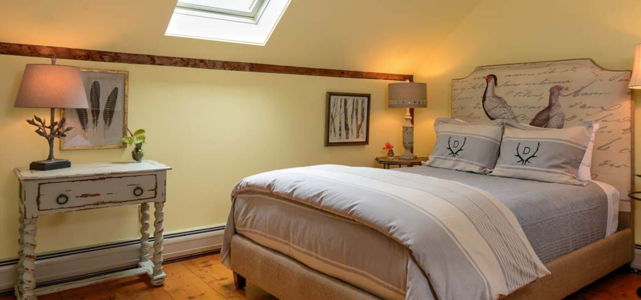 A bedroom with a bed, two bedside tables, a nightstand, a skylight, and wall art.