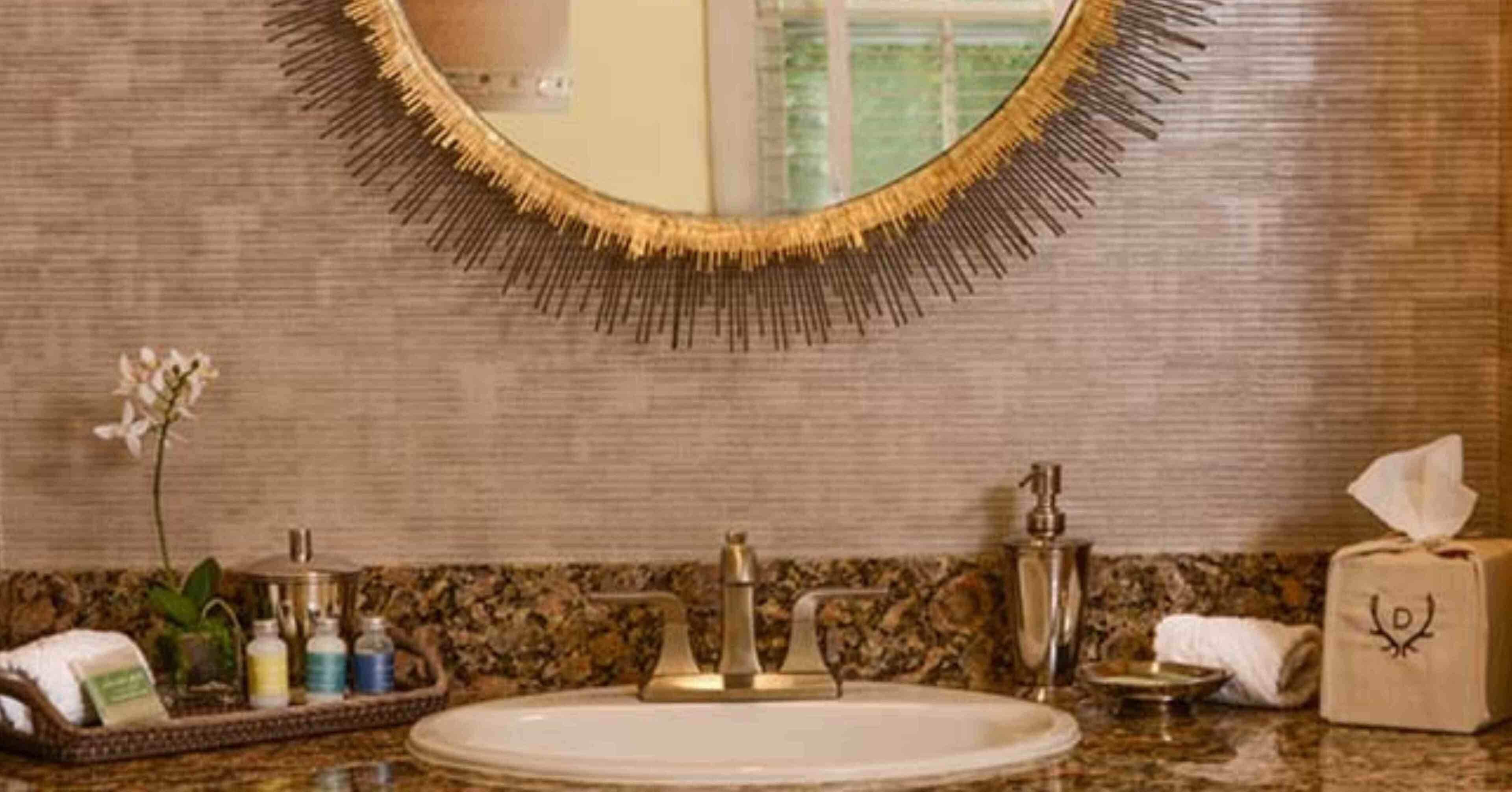 A bathroom with a round mirror, granite countertop, and toiletries.