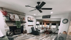 Una sala de estar amplia con chimenea, ventilador de techo y un cartel que dice 'Welcome'.