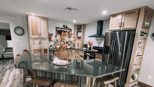 Una cocina moderna con una isla central, taburetes de madera y un refrigerador de acero inoxidable.