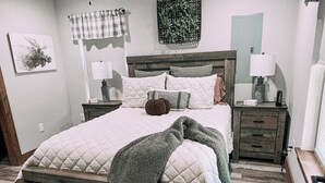 Un dormitorio con cama de madera, ventilador de techo, mesita de noche con lámpara y una obra de arte colgada en la pared.